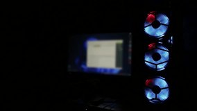 Multi-colored cooling cooler in a computer system unit against the background of a monitor. Rotating multi-colored coolers in a gaming computer. Copy space for text