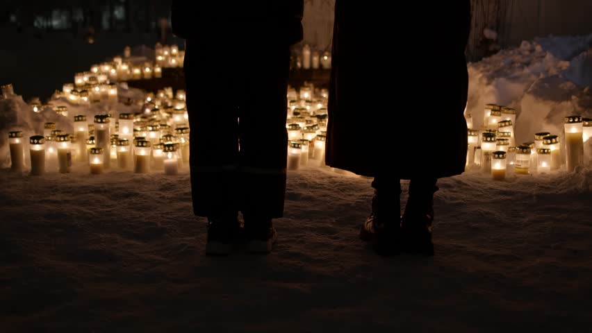 Two girls' silhouettes at the backdrop of candle lights on graves and tombstones at a cemetery. Lit candles illuminate the graves at a Christian cemetery at night. In the memory of victims of the war  Royalty-Free Stock Footage #3405801833
