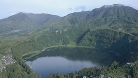 Aerial view of Telaga Menjer, Wonosobo, Indonesia. Green water lake surrounded by green trees of forest and mountain range landscape. Lakes originating from the crater filled with water