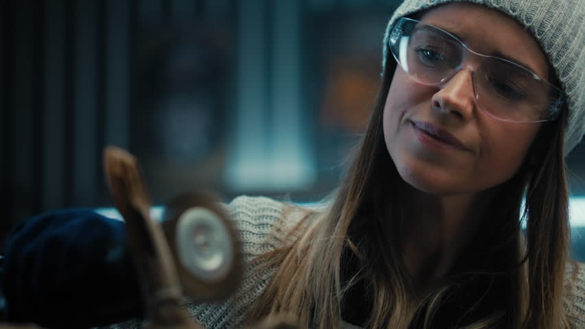 Young woman artisan wearing protective glasses grinds tree branch using grinder. Creative female carpenter woodworking, makes wooden products in stylish garage workshop. Handmade concept. Close up.