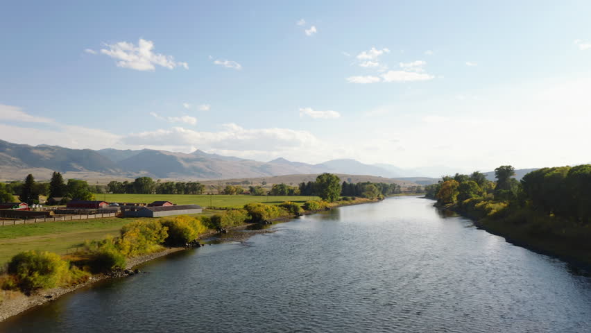 Forwards fly above river in autumn rural landscape. Color foliage on vegetation on riverbanks. Scene lit by sun at golden hour. Montana, USA