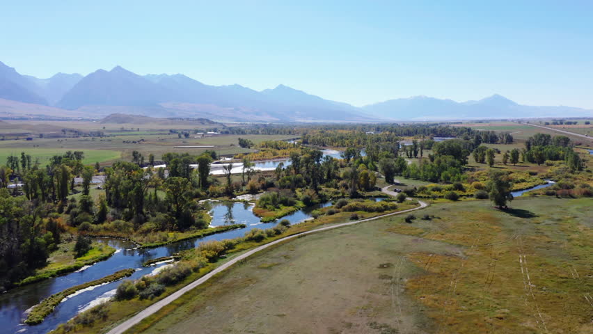 Fly above flat landscape with water course and trees. High mountain ridge in background. Montana, USA