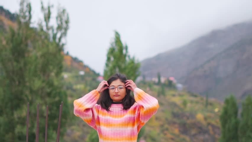 Portrait of young Indian woman staring at camera with expressionless face while standing against mountains in Lahaul, Himachal Pradesh, India. Female with blank expression. Indian ethnicity woman.
