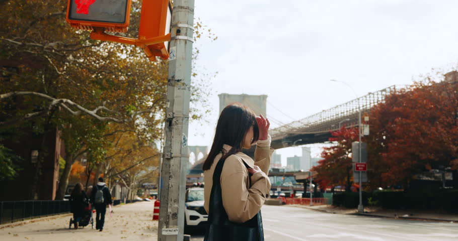 Stylish young brunette woman road crossing and enjoying beautiful view of the Brooklyn Bridge in autumn