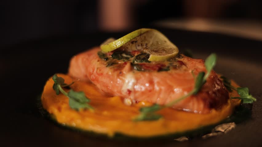 Chic serving of tasteful dish with smoked salmon laying on mashed carrots puree and decorated with fresh pea sprouts on black round plate. Advertisement of high cuisine menu of luxury restaurant.
