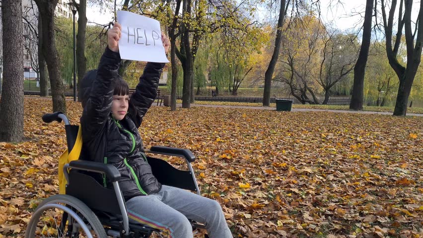 Child girl with text help in wheelchair in park. Child beggar asking for alms