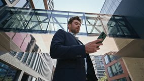 Confident entrepreneur looking cellphone screen on sunny street bottom view. Elegant businessman reading phone message standing urban area. Handsome company owner browsing smartphone app outdoors. - Powered by Shutterstock - Get 15% off with code: PIKWIZARD15