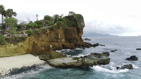 Drone shot on Papuma Beach, Jember, Indonesia with thick vegetations, towering cliff and ocean waves.