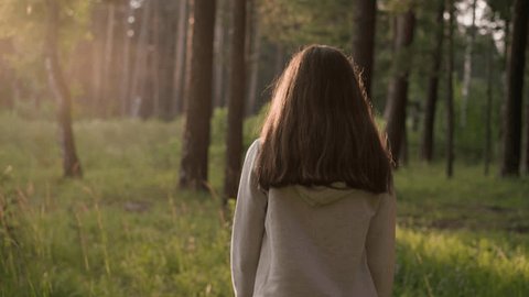 Lonely woman walking through sunny forest. Female walks alone surrounded by trees and wild environment at sunset. Lady feels empty and useless Video Stok