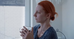 Cosy Coffee Moment: Close-Up of Red-Haired Girl Sipping Coffee, Lost in Thought - 4K Video of Serene Kitchen Ambiance and Reflection