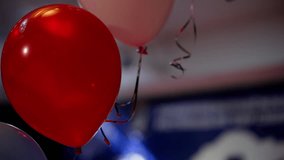 Red and white balloons with ribbons against a stage background with lighting.