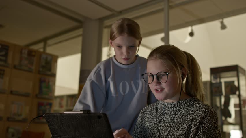 Two young girls surfing web pages in a room on a tablet computer Royalty-Free Stock Footage #3406375869