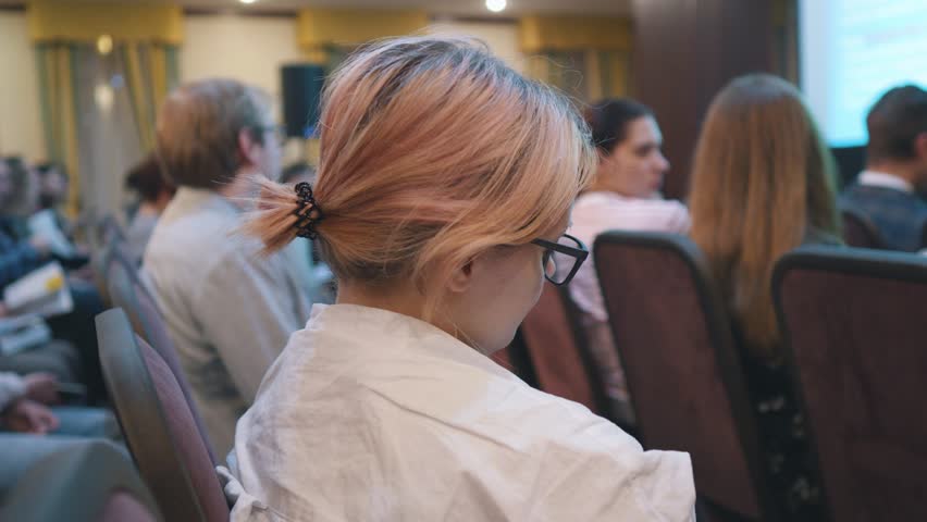 Female student with pink hair in glasses on a lecture in the auditorium.