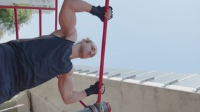 Strong male athlete in sportswear doing chest-to-bar pull ups during street workout outdoors on summer day. Vertical format video