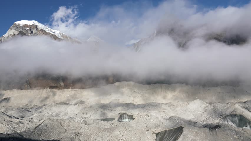 Mysterious fog is spreading over Ngozumba glacier in Himalayan Mountains in real time. Trekking in Nepal to Everest Base Camp via Gokyo Lakes. Clouds moving fast across sky. Weather changes quickly