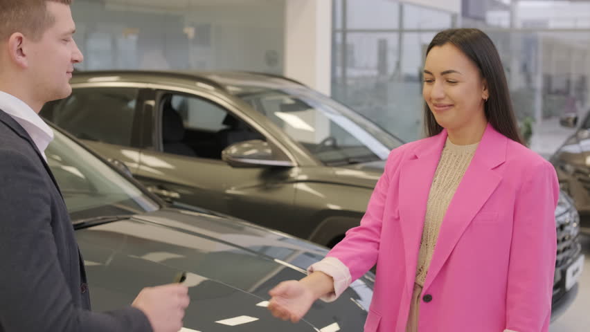 Male hand gives a car keys to female hand in the car dealership close up. Dealer giving key to new owner in auto show or salon.
