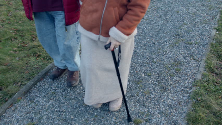 An elderly couple strolling with the support of a cane. Issues such as joint stiffness, muscle weakness, balance concerns associated with aging. Overall mobility and independence of seniors. No face. Royalty-Free Stock Footage #3406627575