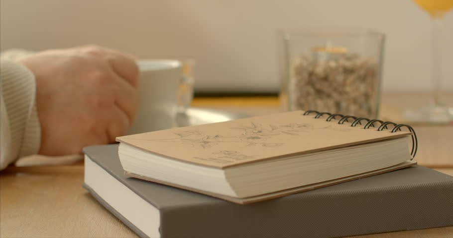 Close-up of books resting on a table in a cafe. Intellectual exploration and relaxation background. Sketchbook represents a personal and expressive space where ideas come to life. Royalty-Free Stock Footage #3406631929