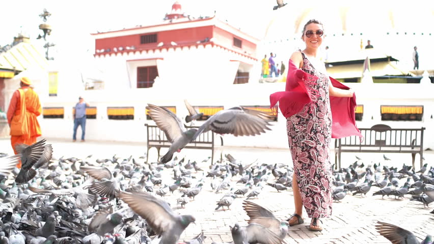 Slow-motion video of woman rotating in middle of oriental square in Kathmandu, Nepal with pigeons taking off in flurry. Lifestyle, animals, traveling concept. Boudhanath Stupa in Kathmandu, Nepal.