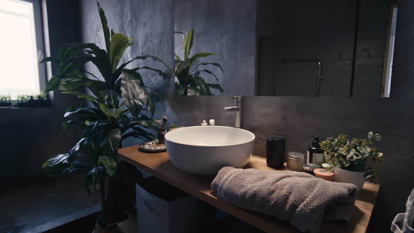 No people side medium footage of modern dark grunge loft bathroom with mirror, table top wash basin, open shower room, skincare products and houseplants Royalty-Free Stock Footage #3406665099