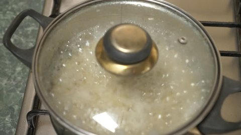 Preparation of brown rice. Boiling water with cereal in a saucepan on the stove. 4k, slow motion