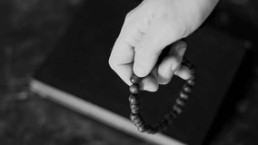 A male hand is fingering a wooden rosary during a close-up prayer black and white video