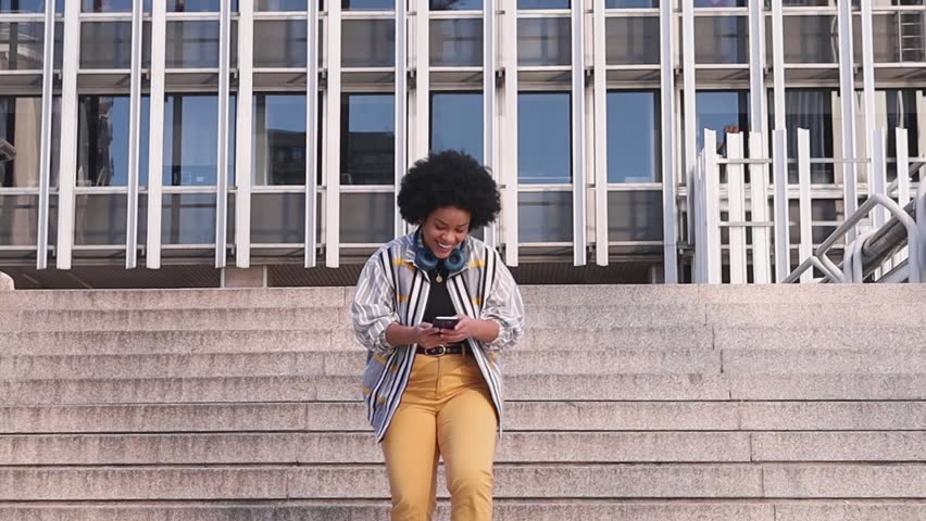 millennial afro woman talking in her phone in stairs