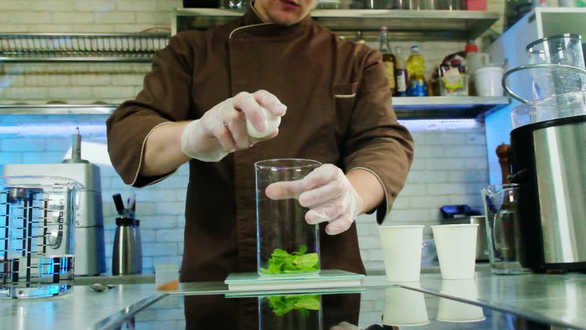 Skilled culinarian cracks chicken egg into transparent measuring cup with spinach. Process of making new gastronomy treasure