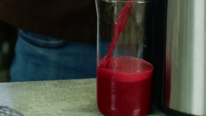 Beet-root juice pouring into transparent jug from juice maker. Kitchen worker makes vitamin drink with professional kitchen equipment