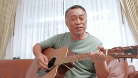 Elderly Asian man playing guitar and singing at home He is happy with his retired life. music concept, live performance