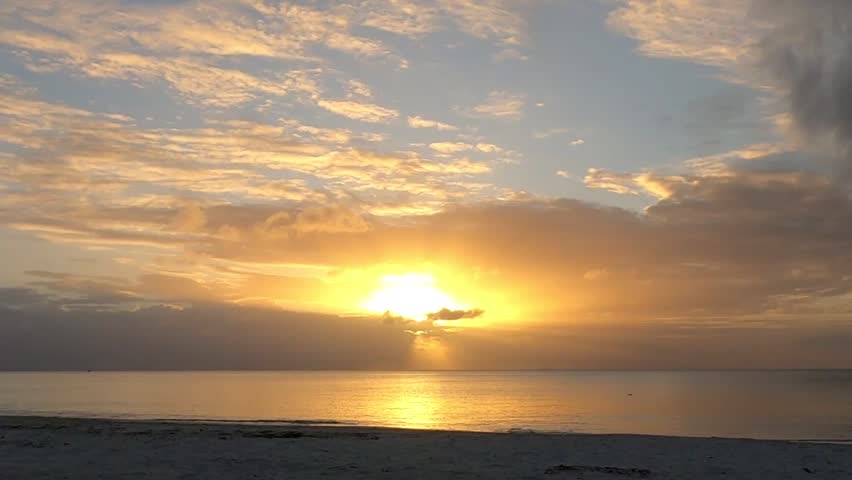 Sun setting behind clouds above calm ocean.