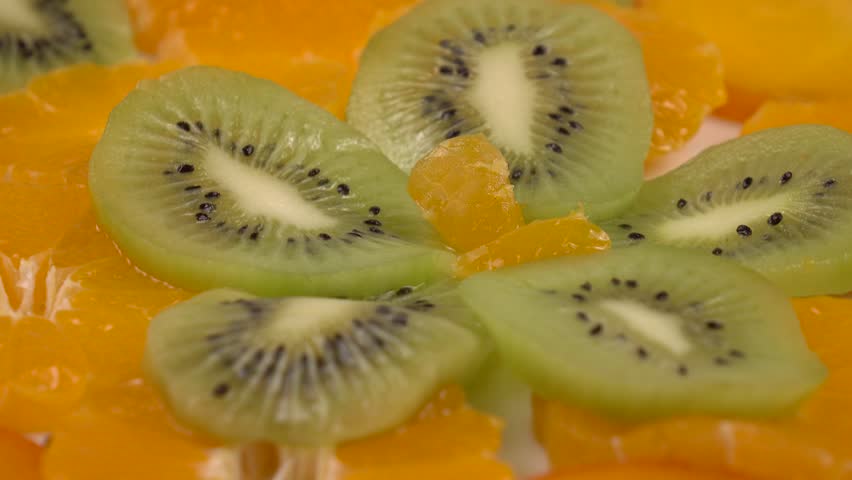 Slices of ripe peeled tangerines, persimmons and kiwis are laid out on a plate. Vitamin fruit dessert, background