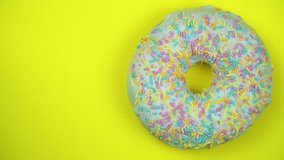 Delicious sweet donut rotating on a plate. Top view. Bright and colorful sprinkled donut close-up macro shot spinning on a yellow background.