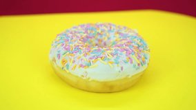 Delicious sweet donut rotating on a plate. Top view. Bright and colorful sprinkled donut close-up macro shot spinning on a yellow background.