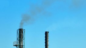 In a clear blue sky, an industrial plant emits black smoke, illustrating the ongoing battle against air pollution endangering our environment. Greenhouse gases and Carbon monoxide concept. Aerial.
