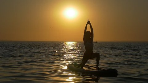 Yoga exercises on the paddle board. Girl takes yoga on the water at dawn