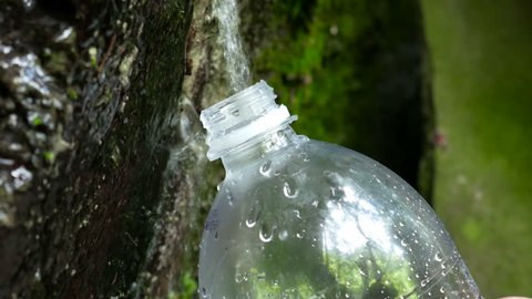 Man refills clear drinkable water from stone source spring into plastic bottle for later using at walk on treck Arkivvideo