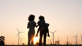 Silhouettes of Happy family father, mother and child daughter sits on the shoulders of his father with windmills for electricity generation at sunrise by producing sustainable energy. 4k video