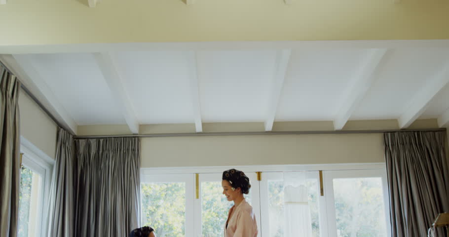 Excited bridesmaids in nightdress and hair rollers tossing a glass of champagne at home 4K 