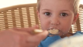mother feeds porridge to her son. happy family healthy food concept. the boy little son eats porridge with a spoon soiled in his face lifestyle. child dirty funny eating porridge himself video