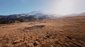Low flight of a sports FPV drone at high speed high in the mountains over a yellow autumn field surrounded by snow-capped mountains of the Caucasus mountain range and Elbrus volcano - Powered by Shutterstock - Get 15% off with code: PIKWIZARD15
