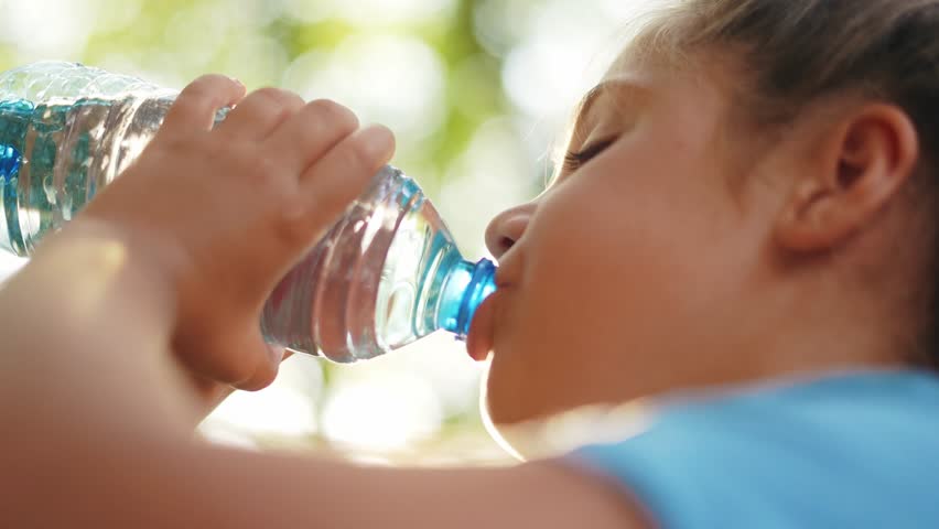 child drinking water from a plastic bottle. water shortage problem on earth concept. water shortage problem on earth concept. kid lifestyle drinks water in nature from a bottle glare of the sun summer
