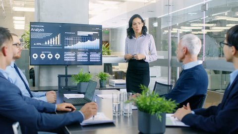 Beautiful Businesswoman Gives Report Presentation to Her Business Colleagues in the Conference Room, She Shows Graphics, Pie Charts and Company's Growth on the Wall TV. 