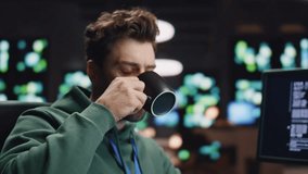 Overworked data center analyst drinking coffee coding at computer workplace. Tired coder working monitors in advanced monitoring office closeup. IT engineer man sipping beverage taking break at work - Powered by Shutterstock - Get 15% off with code: PIKWIZARD15