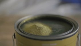 This video shows a close up view of metallic gold metal flakes being added into a paint bucket in slow motion.