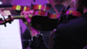 A close-up of a violinist performing on stage. Violin in the hands of a professional musician of a symphony orchestra, playing on the stage of a classical theatre. Blurred video