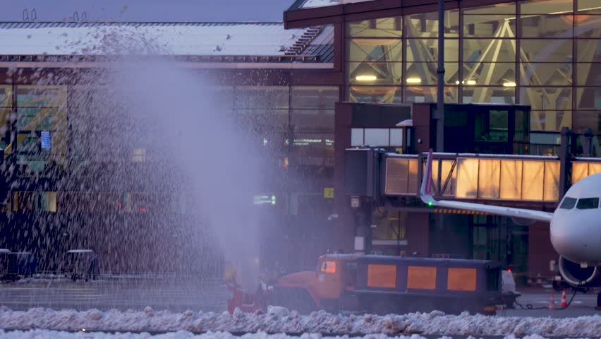 Big orange snow plow truck removes clearing cold snow at international airport terminal and runway after severe arctic outflow and snowstorm in area Slow motion. Bad weather, snow-clearing machinery
