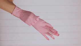 Vertical video of hands wearing a pink latex glove. Two hands of a woman wearing gloves on a white background. Prevention of viral diseases.