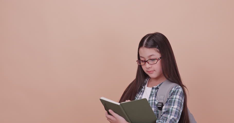 Schoolgirl thinking something and write it down in a notebook. Isolated on brown background in studio.
