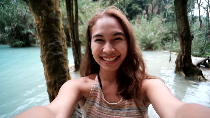Cheerful enthusiastic Asian tourist girl happily turn around in Kuang Si waterfall, Luang Prabang, Laos. Young woman have fun and happy sightseeing with nature. (Selfie shot) Royalty-Free Stock Footage #34083241